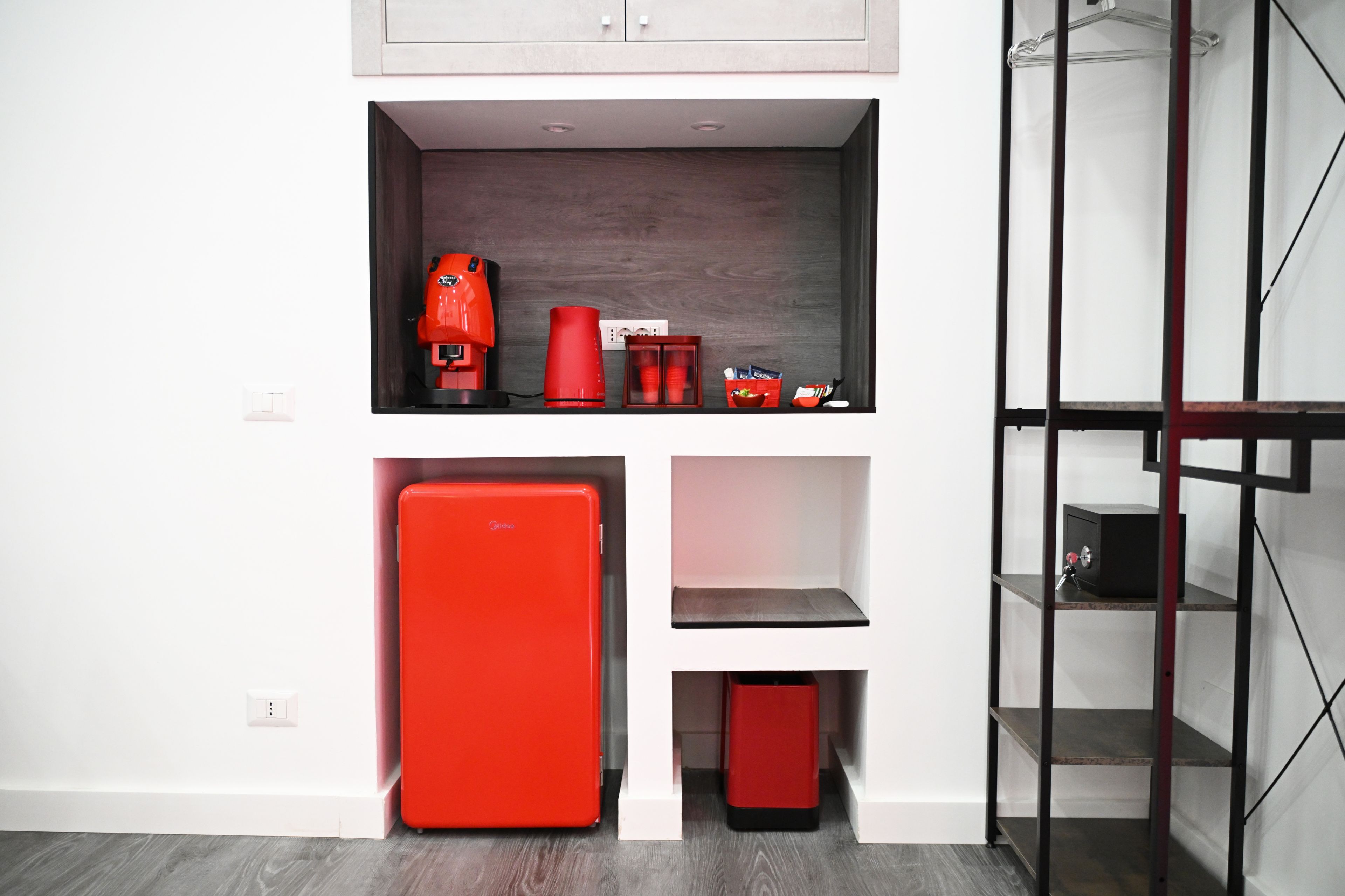 Una cocina compacta con un refrigerador rojo integrado, una cafetera y un lavamanos pequeño.