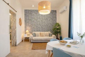 Ein modernes Wohnzimmer mit einer Couch, einem Esstisch mit einer Schale Snacks, einer Hängeleuchte und einem Blumentopf.