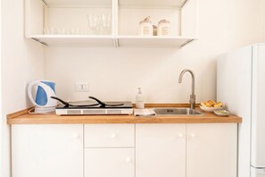 Une cuisine compacte équipée d’un four encastré, d’une bouilloire, d’un évier et d’un plan de travail sur lequel se trouvent un grille-pain et un panier de pain.
