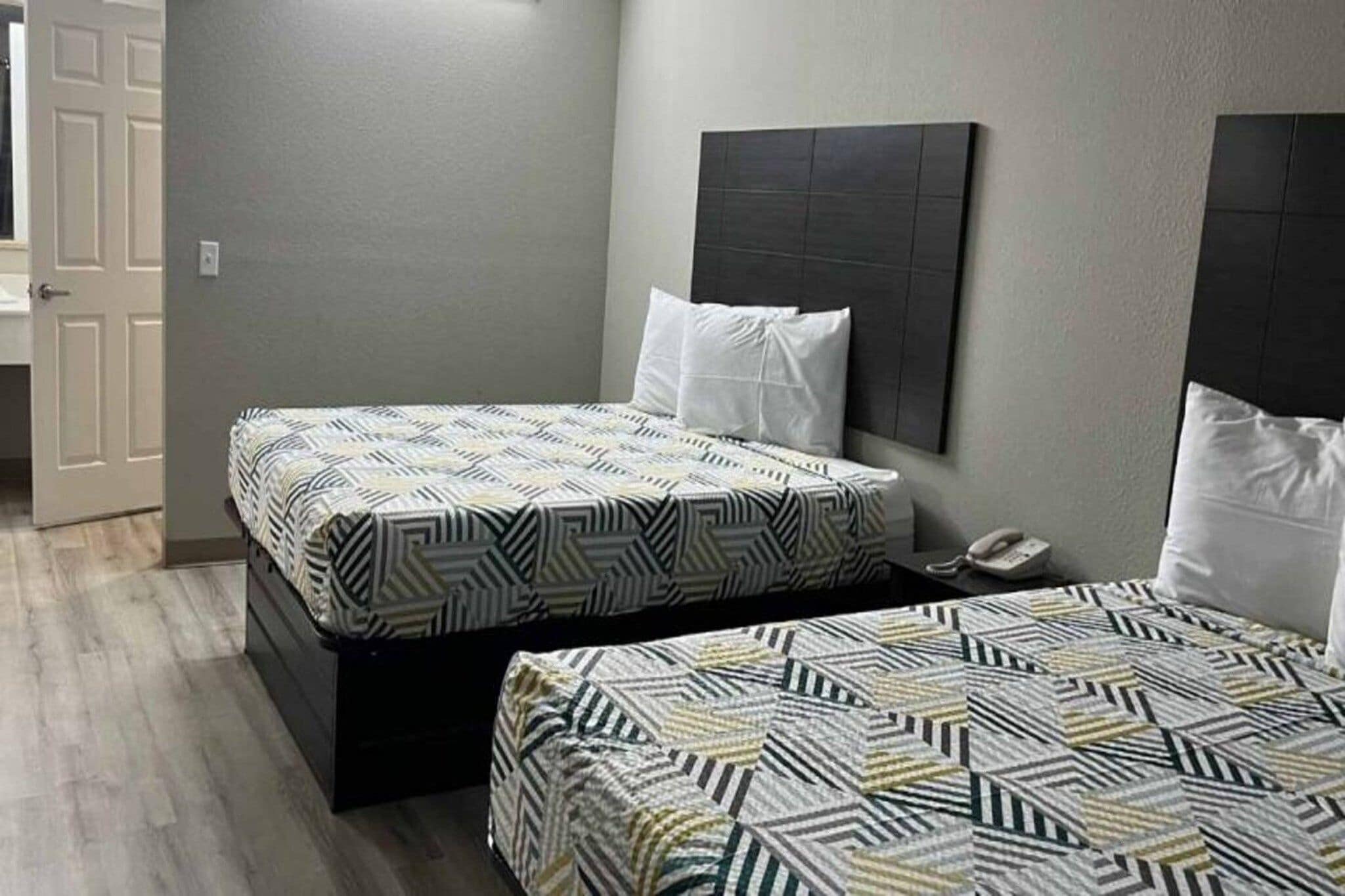 A hotel room with two beds, a bedside telephone, and a door to the left.