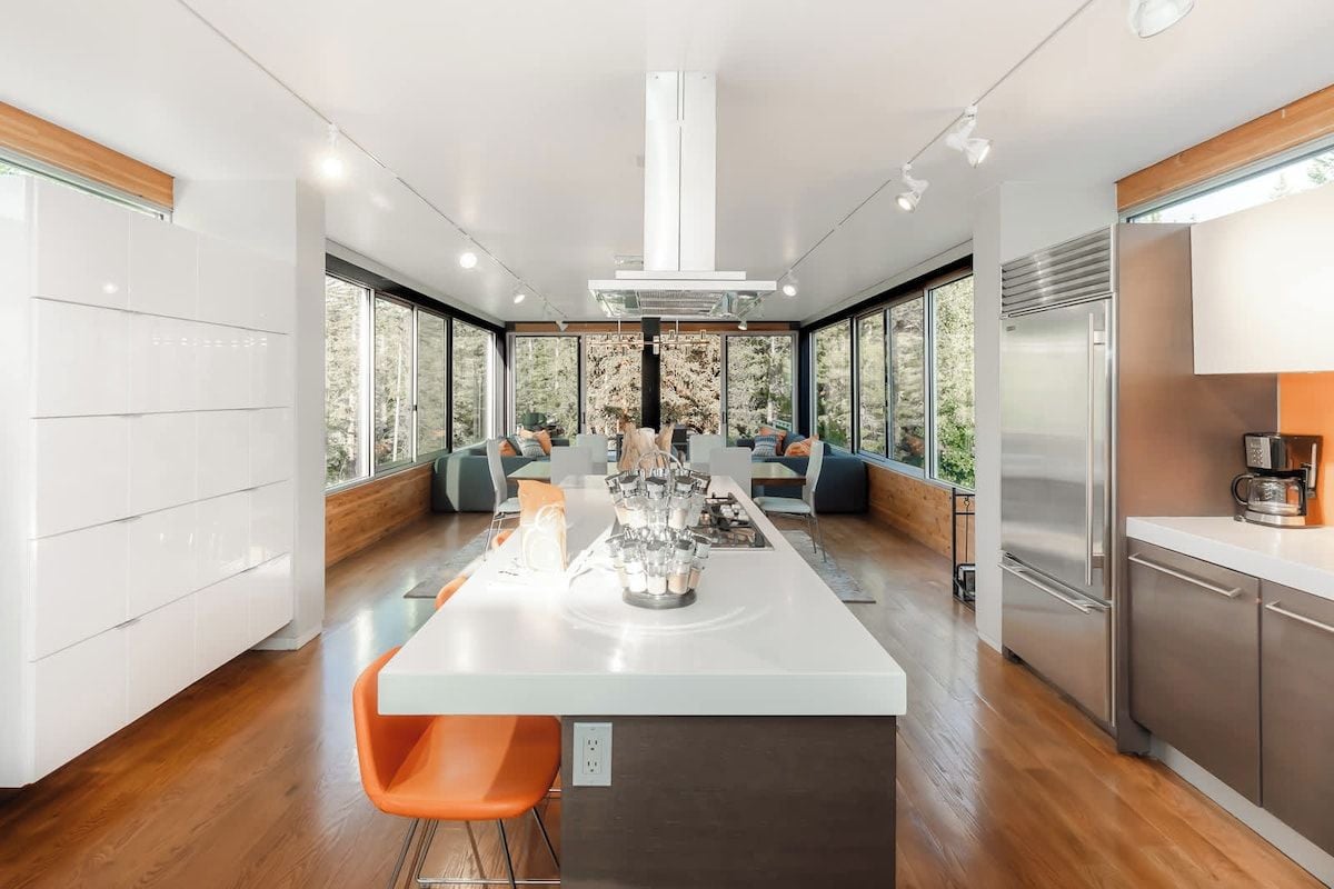 Une cuisine moderne dotée d’un îlot central, d’appareils électroménagers intégrés et de grandes fenêtres offrant une vue sur l’extérieur.