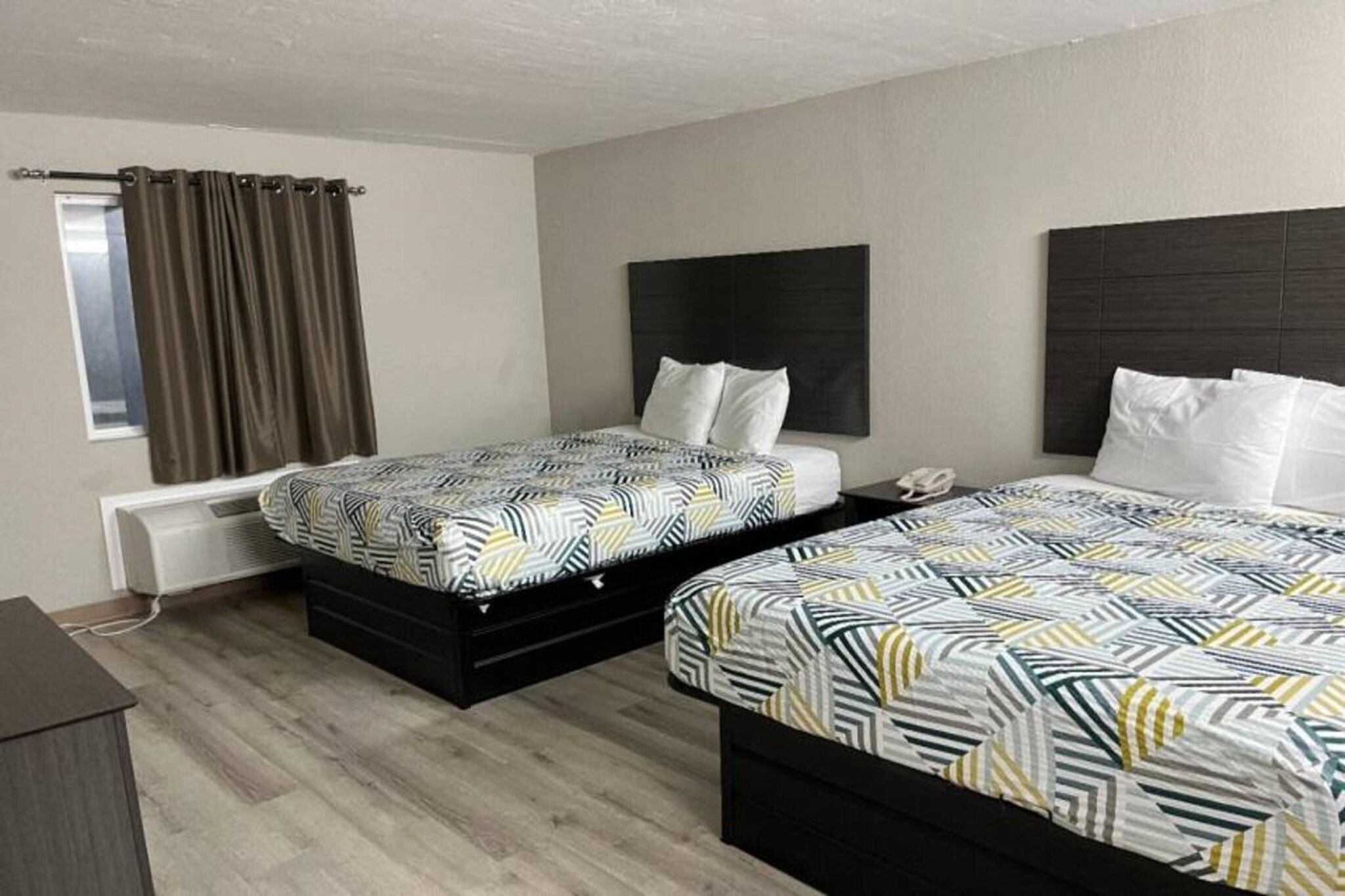A hotel room with two beds, a desk, a chair, a window with curtains, and a wall-mounted phone.