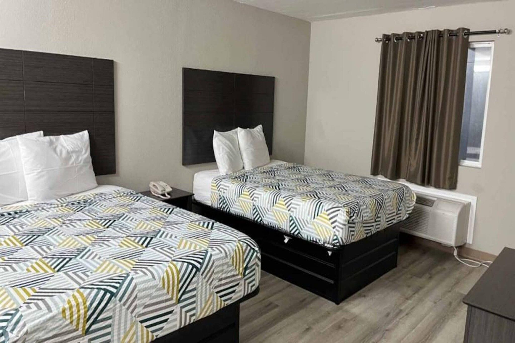 A hotel room with two beds, a bedside telephone, a window with curtains, and a radiator.