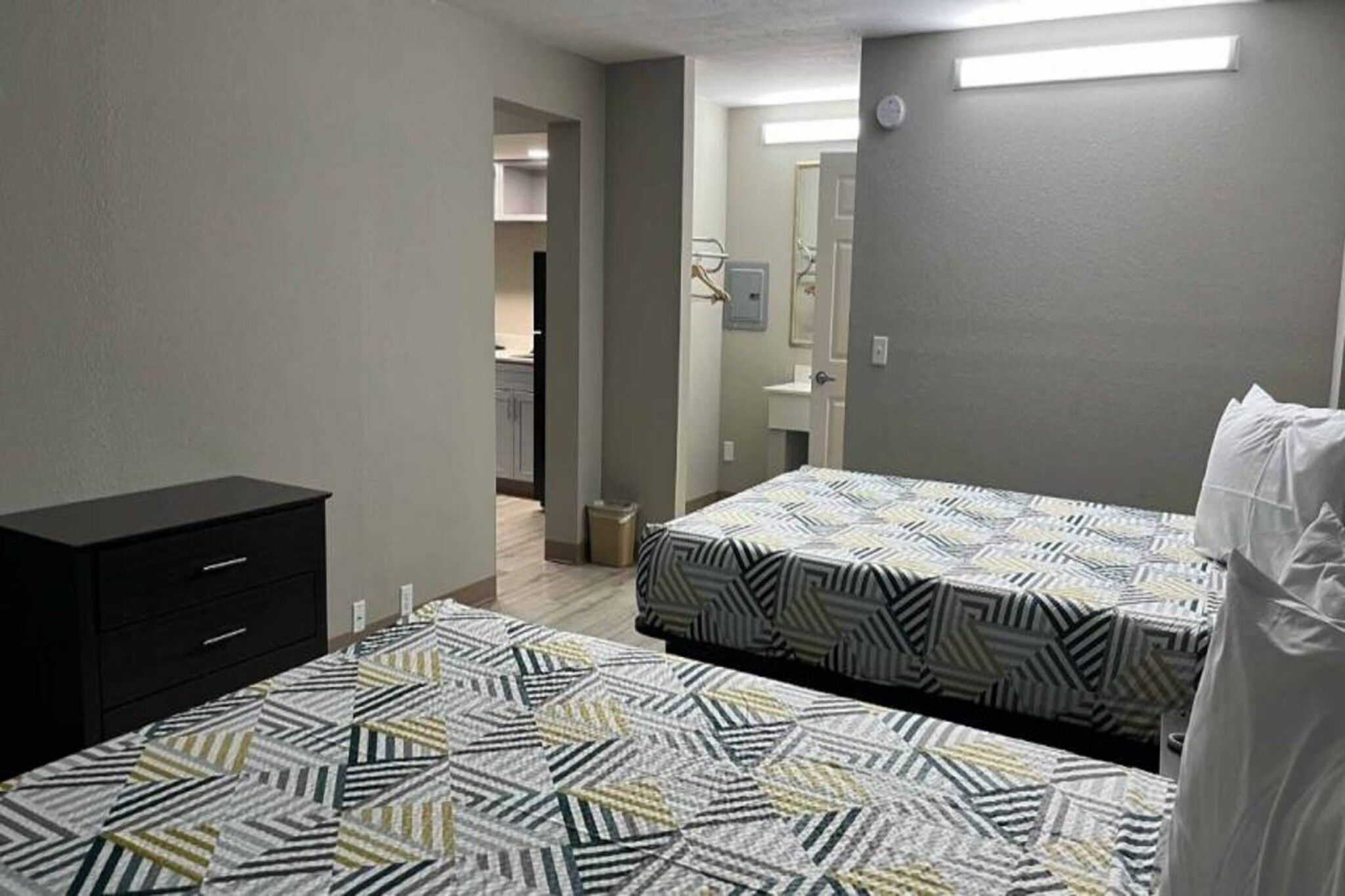 A bedroom with two beds, a dresser, and a bathroom visible in the background.
