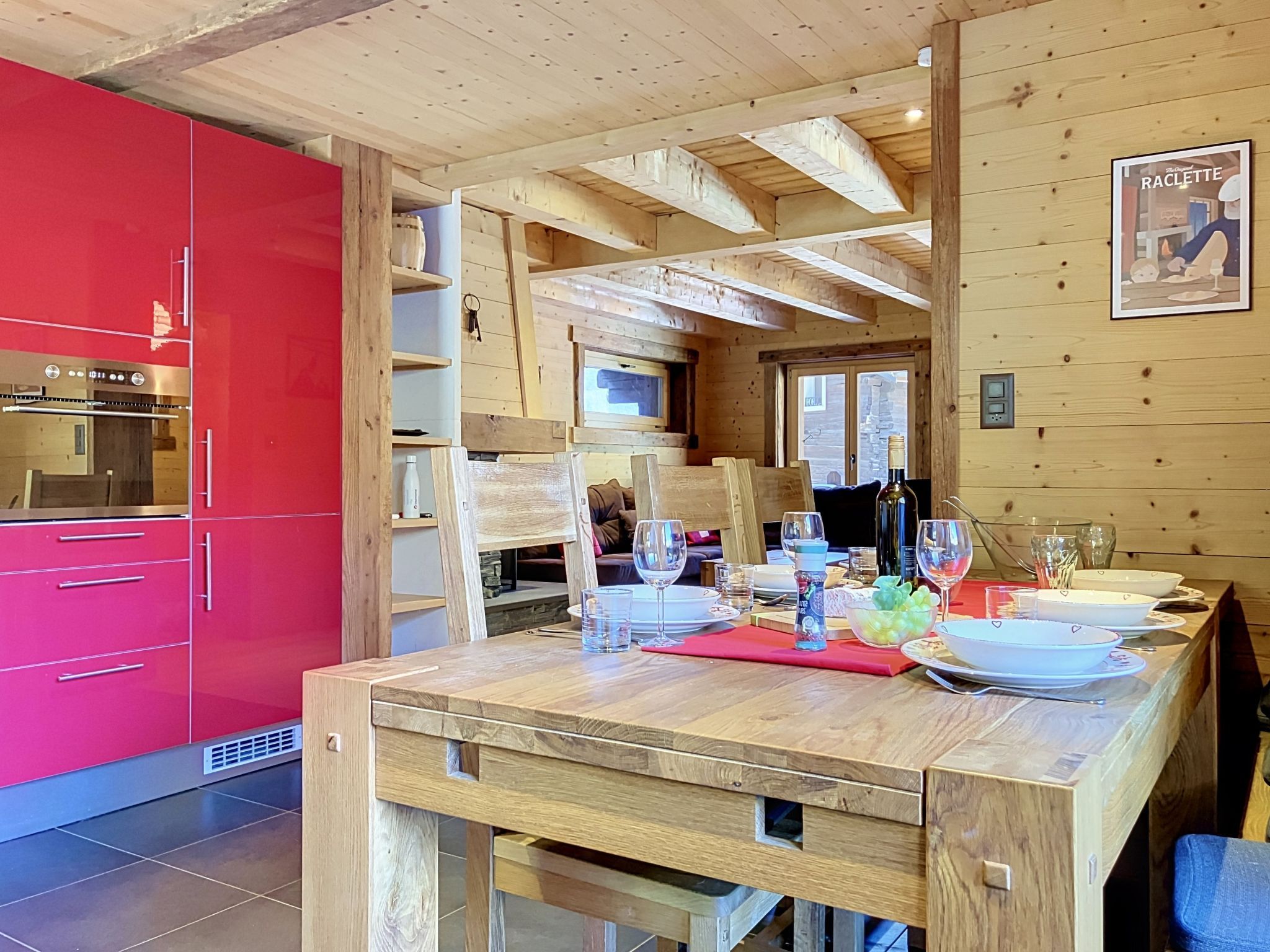 Une table de salle à manger en bois, mise avec des assiettes, des verres et une bouteille, dans une pièce aux meubles rouges et au plafond en bois.