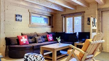 Ein gemütliches Blockhaus-Interieur mit einer Couch, einem Schaukelstuhl, einem Fernseher und einem Fenster mit Blick.
