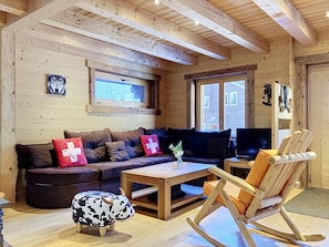 Ein gemütliches Blockhaus-Interieur mit einer Couch, einem Schaukelstuhl, einem Fernseher und einem Fenster mit Blick.