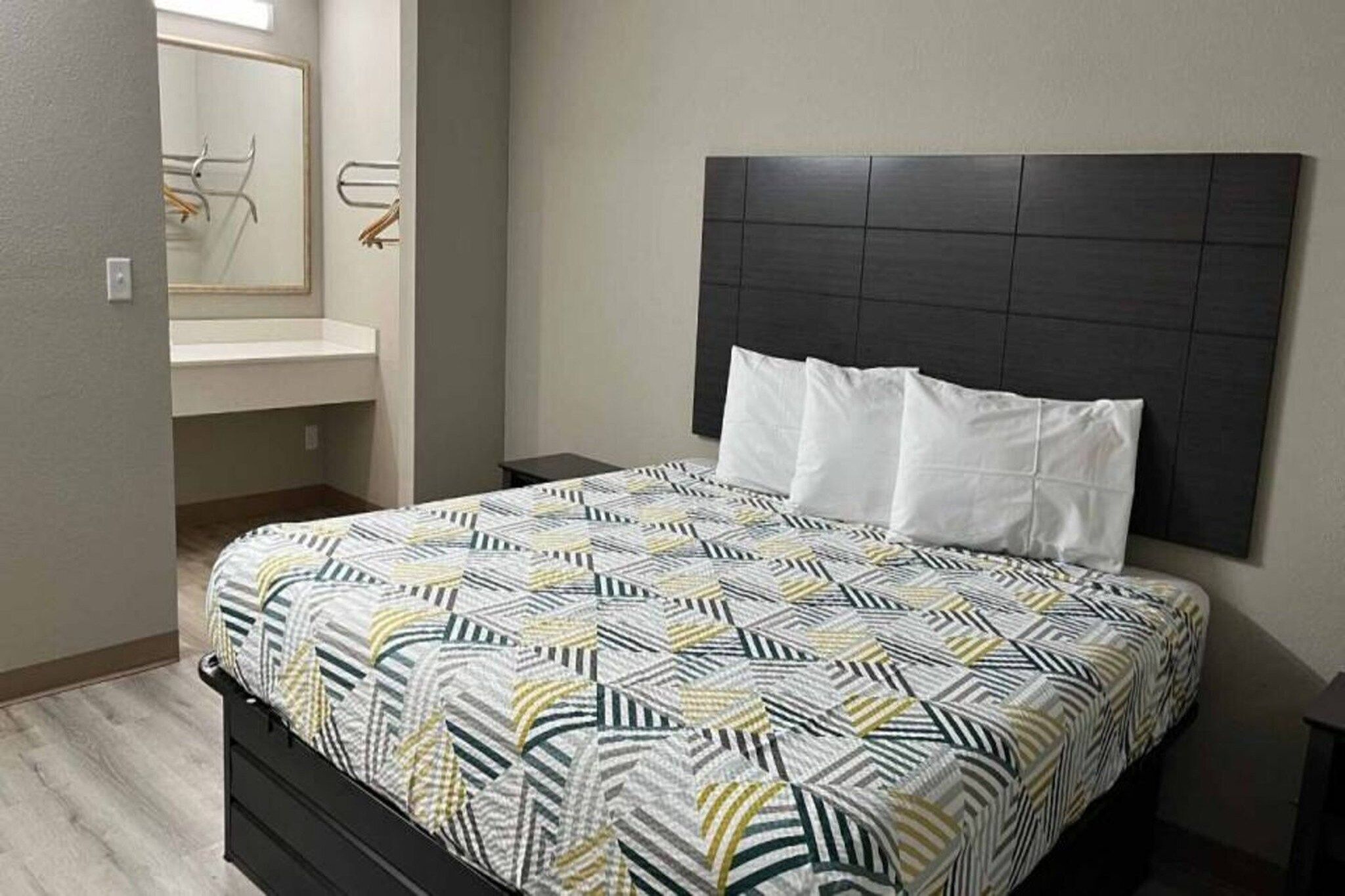 Een hotelkamer met een bed, een hoofdeinde, een nachtkastje, een spiegel en een badkamer met een handdoekhouder.