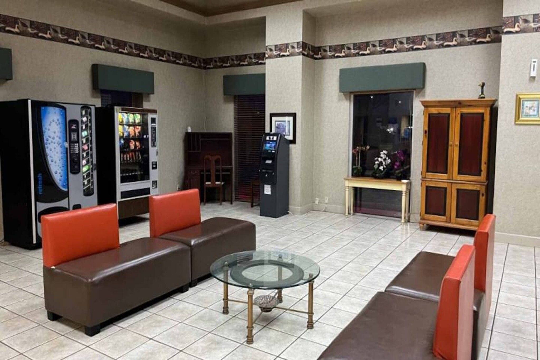 Eine Lobby mit einem braunen Sofa, einem Glastisch, Verkaufsautomaten und einer Holzkassette.