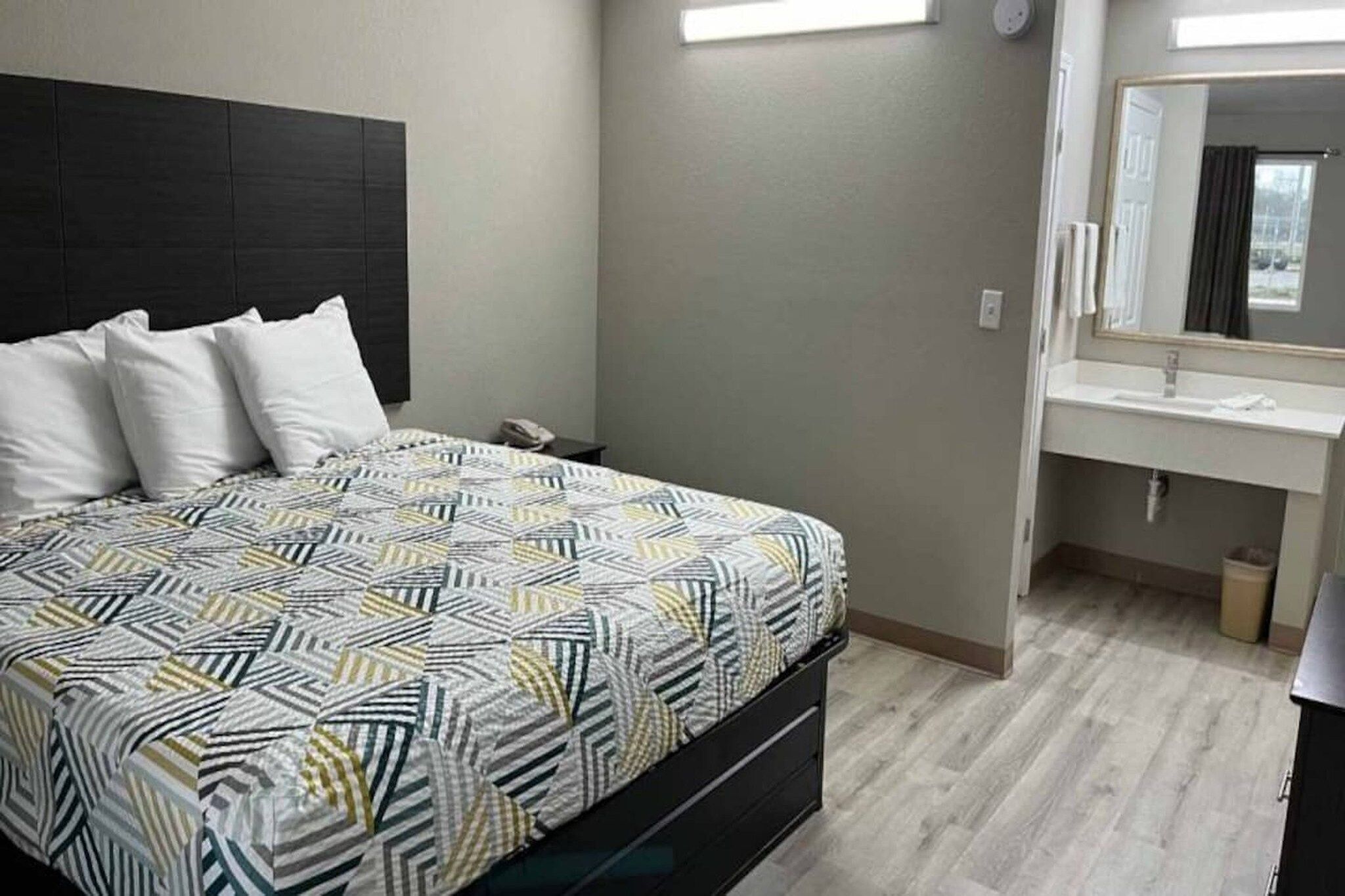 Une chambre à coucher comprenant un lit, une table de chevet, un miroir et une salle de bain avec un lavabo et des toilettes.