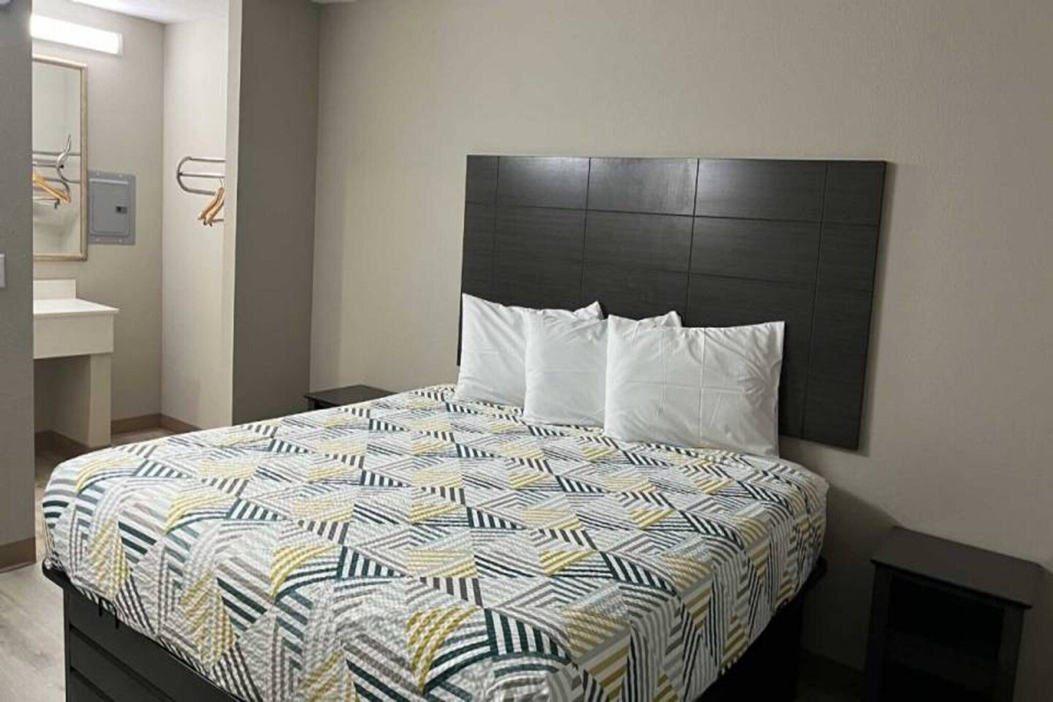 Ein Bett mit einem gemusterten Überwurf, einem dunklen Kopfteil und weißen Kissen.