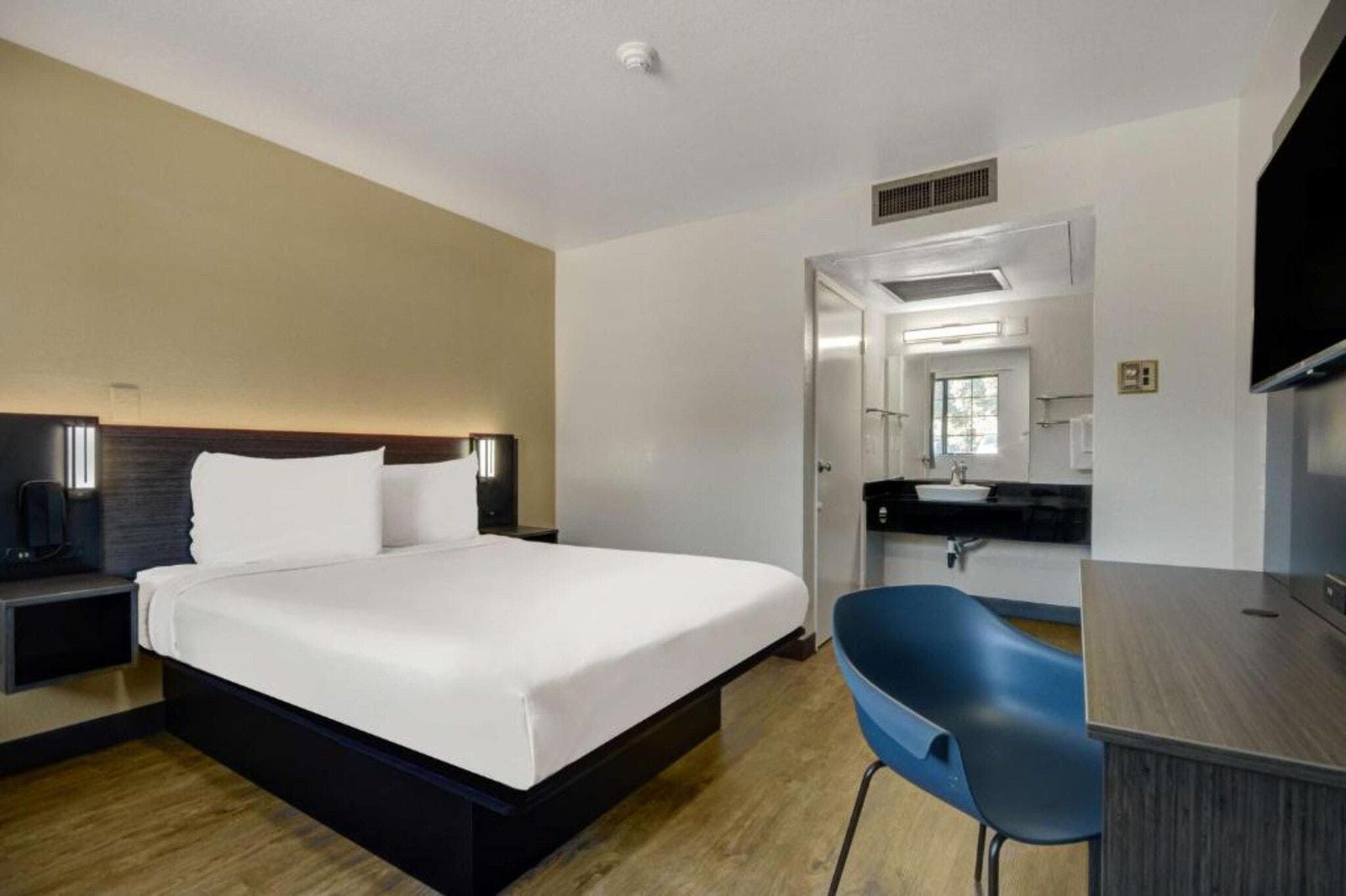A hotel room with a bed, bedside table, desk, chair, and a mirror.
