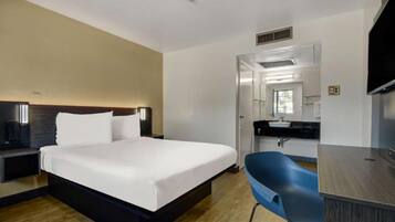 A hotel room with a bed, bedside table, desk, chair, and a mirror.