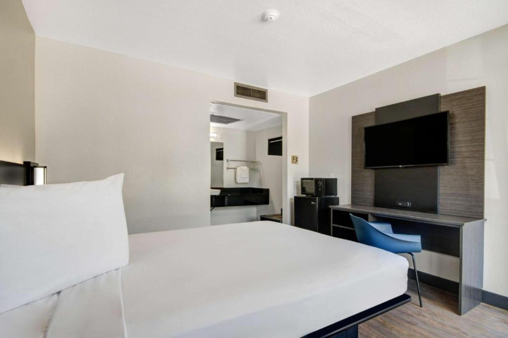 A hotel room with a bed, a desk, a chair, a flat-screen TV, and a mirror.