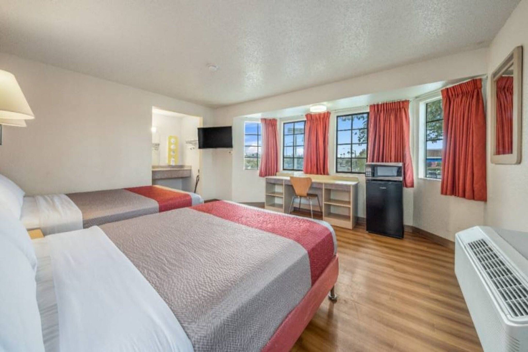 A hotel room with two beds, a desk, a television, and a kitchenette.