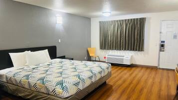 Quarto de hotel com cama, cadeira, janela com cortinas, porta e ar condicionado.