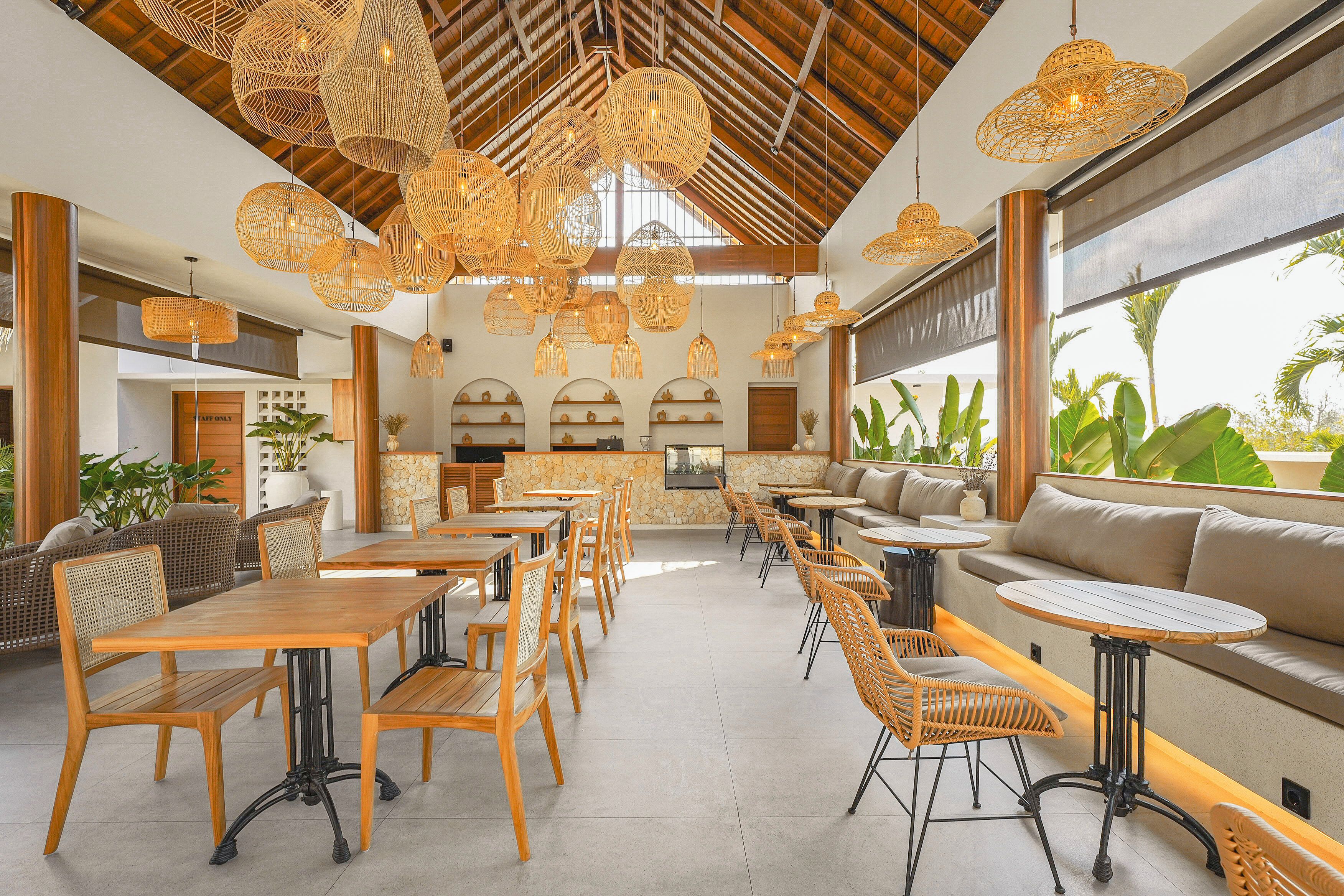 A spacious indoor area with wooden tables and chairs, a stone wall, and a large window overlooking greenery.