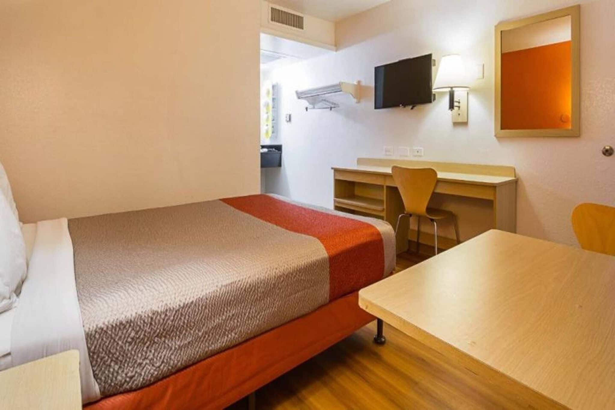 A hotel room with a single bed, a desk, a chair, a television, and a mirror.