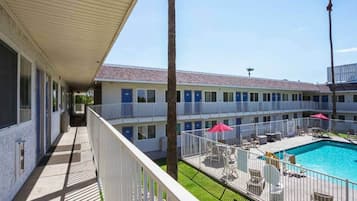 A motel with a pool area, including a fenced deck with chairs and umbrellas.