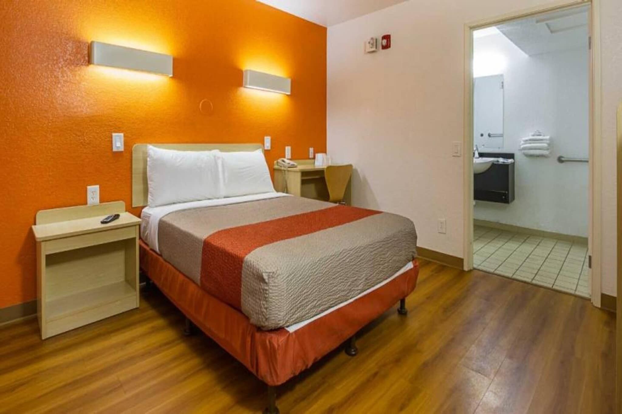 A hotel room with a bed, nightstands, a desk, and a bathroom visible through an open door.