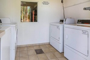 Een wasserette met twee wasmachines, een droger en een bord met de tekst 'Motel is niet verantwoordelijk voor achtergelaten spullen'.
