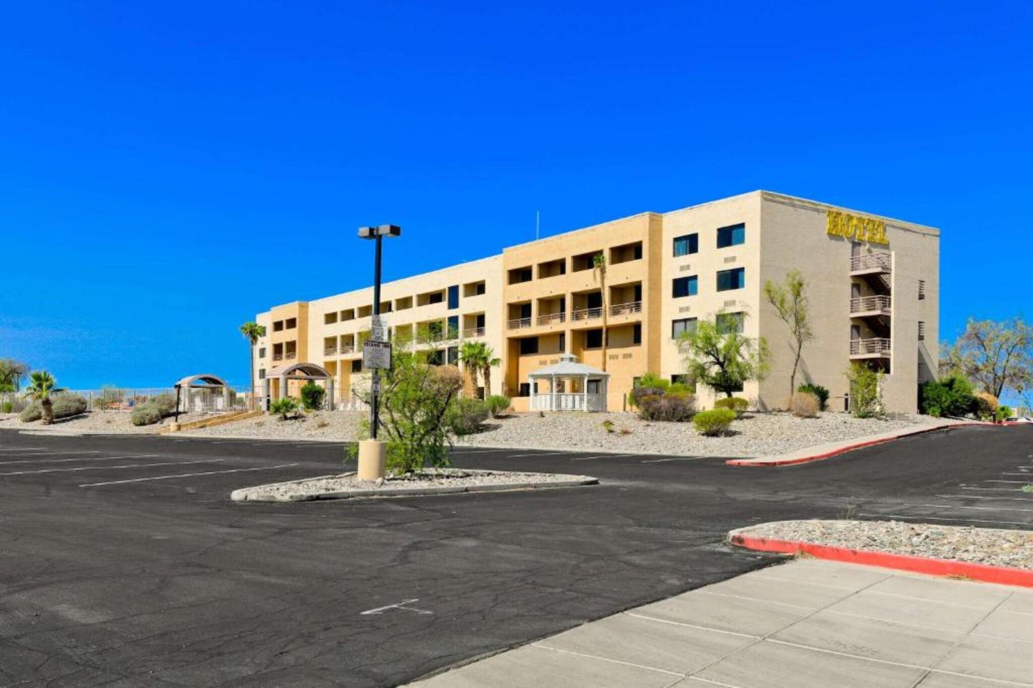 A multi-story hotel with a flat roof, a parking lot, and a clear blue sky.