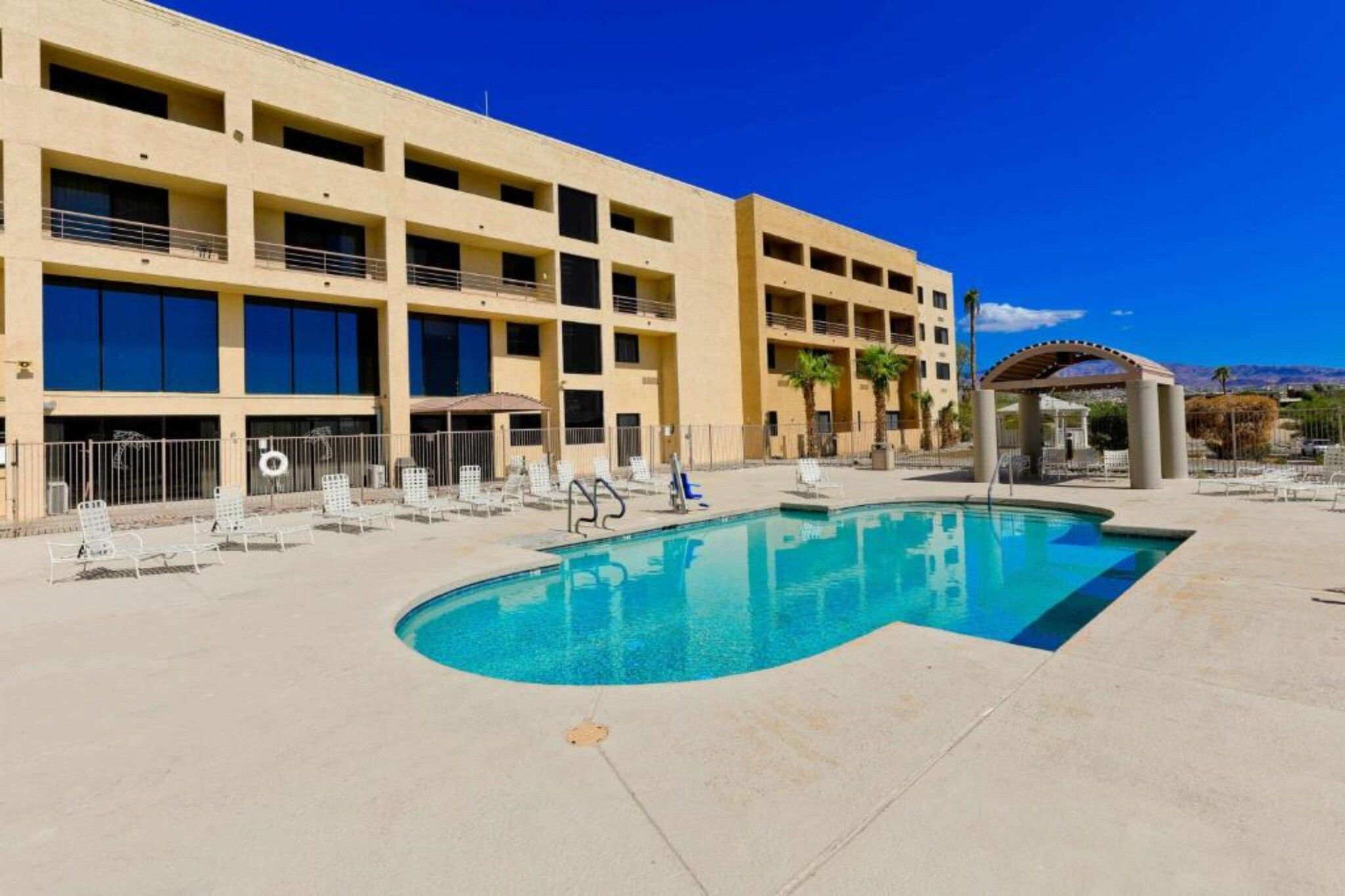 A hotel with a swimming pool, multiple balconies, and a clear blue sky.