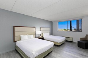A hotel room with two beds, a nightstand with a lamp, a window with a view, and a small seating area. - 2 Queen Beds | Non-Smoking, Micfridge (Lake Havasu City)