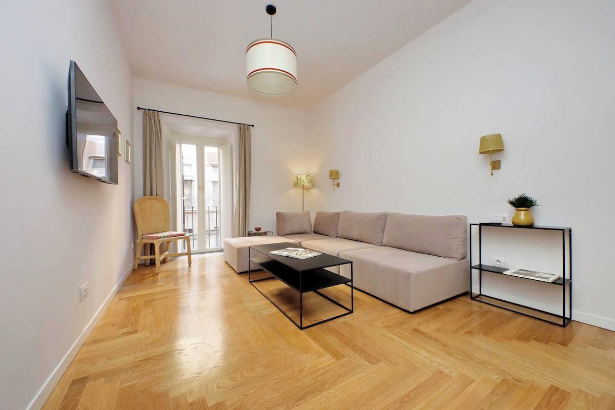 Ein modernes Wohnzimmer mit einer Couch, einem Couchtisch, einem Sessel, einem Fernseher und einem Bücherregal.