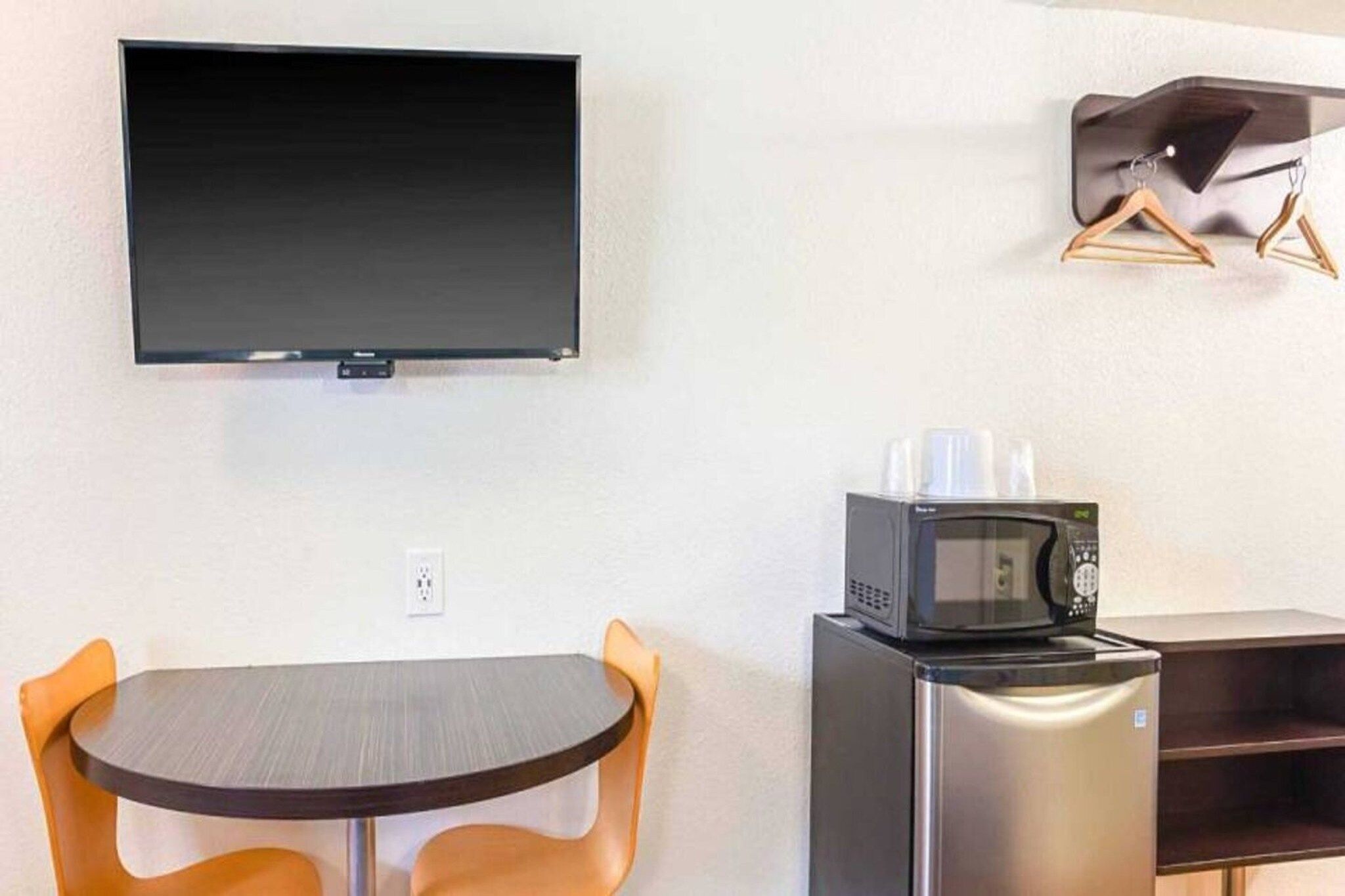 A kitchenette with a microwave, a small refrigerator, a table with two chairs, and a flat-screen TV mounted on the wall.