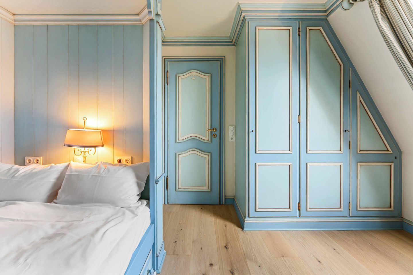 Une chambre à coucher comprenant un lit, une table de chevet, une lampe et une armoire avec une porte.
