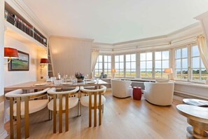 A dining area with a table set for four, a sofa, and a view of the outdoors through large windows. - Twee Seen 33 - "Twee Seen 33" Vacation Rental (Kampen (Sylt))