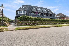A modern house with a sloped roof, a stone retaining wall, and a paved driveway. - Twee Seen 33 - "Twee Seen 33" Vacation Rental (Kampen (Sylt))