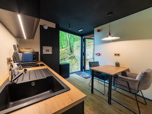 A modern kitchen with a sink, wooden countertop, and a dining area with a table and chairs. - The Serene Escape - Olivenise Cabin (La Roche-en-Ardenne)