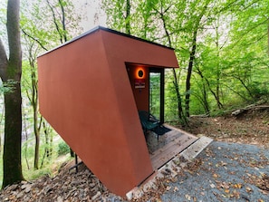 A modern, red, geometric structure with a bench and a door, surrounded by a forested area. - The Serene Escape - Olivenise Cabin (La Roche-en-Ardenne)