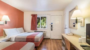 Een hotelkamer met twee bedden, een bureau, een stoel, een televisie en een raam met gordijnen.