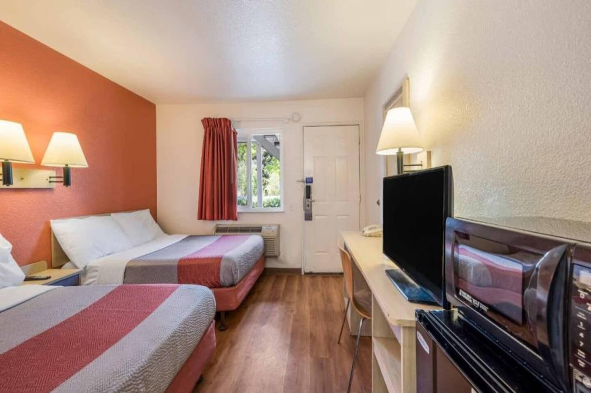 A hotel room with two beds, a desk with a television, and a microwave.