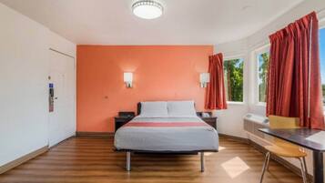 A hotel room with a bed, a desk, and a window with curtains.
