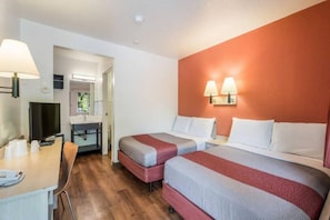 Een hotelkamer met twee bedden, een bureau met lamp, een televisie en een badkamer met spiegel.
