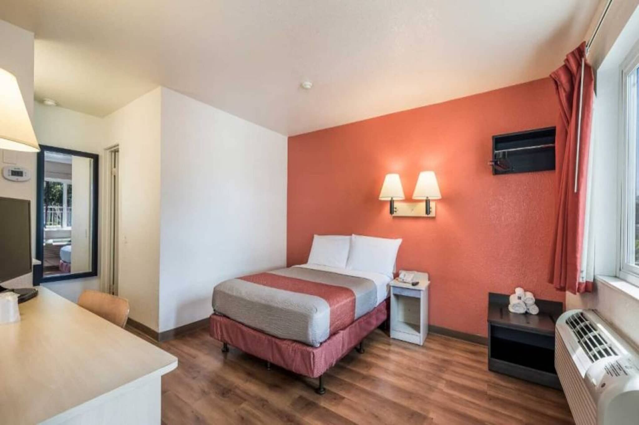 A hotel room with a bed, bedside table, lamp, and a heater.