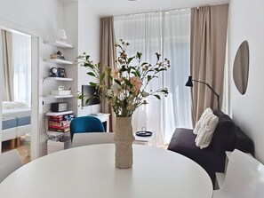 A modern hotel room with a round dining table, a black sofa, a white armchair, a bookshelf, and a large window with sheer curtains. - Franz Josef by Interhome (Bad Gastein)