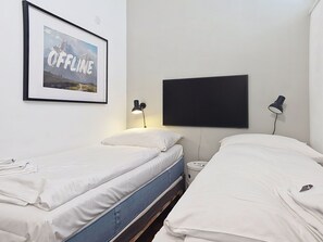 Ett hotellrum med två separata sängar, en inramad tavla på väggen, en platt-TV och två sänglampor.