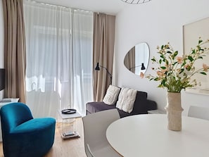 A modern living room with a round dining table, a blue armchair, a grey sofa, and a large window with sheer curtains. - Franz Josef by Interhome (Bad Gastein)