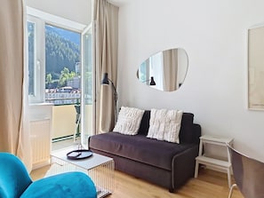 A modern living room with a sofa, a coffee table, a floor lamp, and a view of a mountainous landscape through the window. - Franz Josef by Interhome (Bad Gastein)
