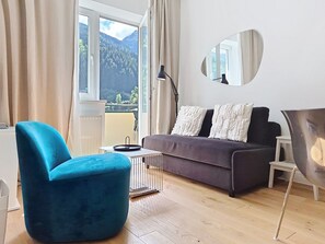 A modern living room with a sofa, a blue armchair, a coffee table, a lamp, and a view of mountains through the window. - Franz Josef by Interhome (Bad Gastein)