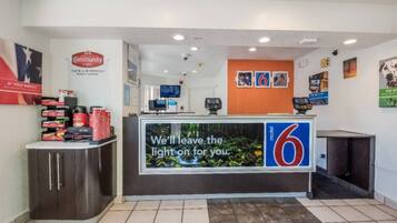 A reception desk with a digital screen displaying a message, a counter with a 6 logo, and a wall with various posters.
