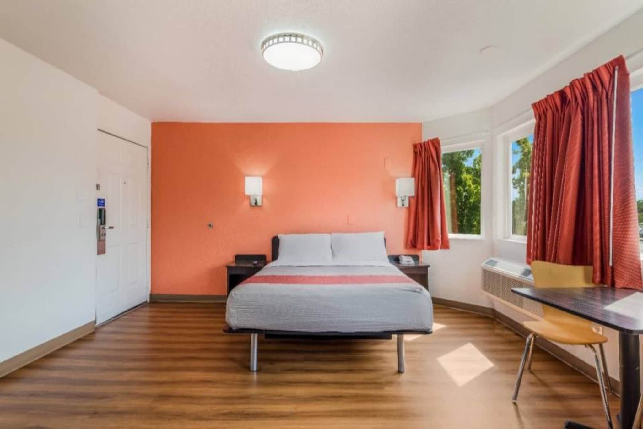 A hotel room with a bed, a desk, a chair, a window with curtains, and a door.