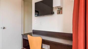 A room with a desk, a chair, a television mounted on the wall, and a door.