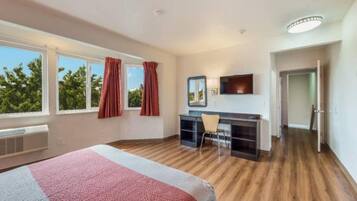 Habitación de hotel con una cama, un escritorio, una silla, un televisor y una puerta que da a otra habitación.