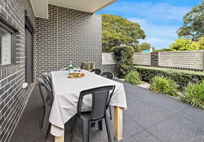Un espacio exterior para comer con pared de ladrillo, una mesa dispuesta con platos, vasos y una botella, y sillas.
